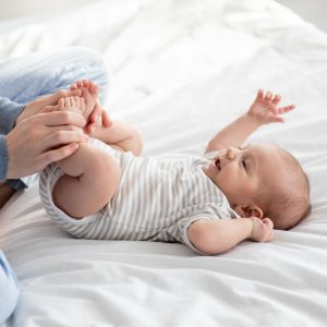 Caring Mother Making Gymnastics To Her Newborn Baby On Bed At Home